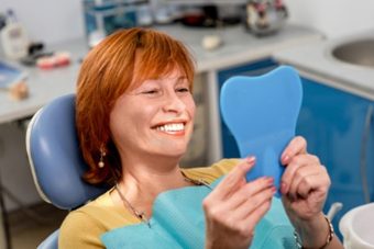Smiling Woman in Dental Chair Looking at her teeth in a mirror | Avalon Dental, your Carson and El Segundo Dentist