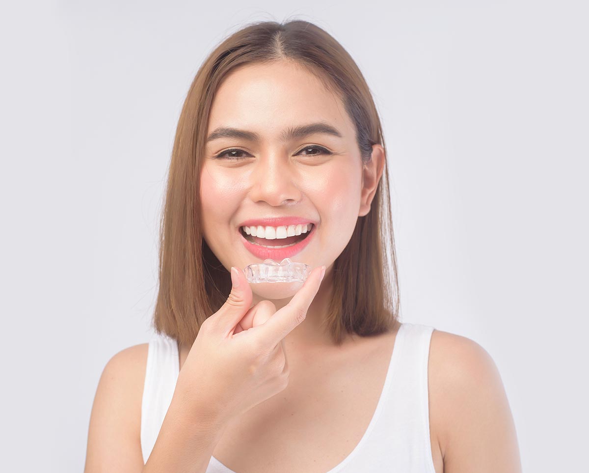 A young smiling woman holding invisalign braces over white background studio, dental healthcare and Orthodontic concept.