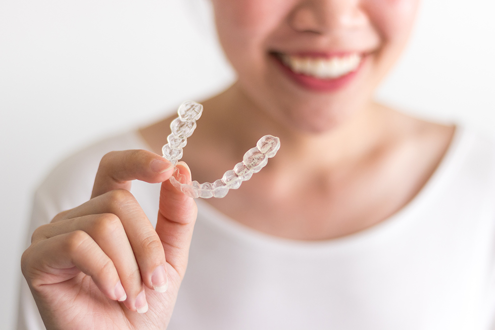 Smiling person holding Invisalign aligners, illustrating the topic of being a good candidate for Invisalign treatment