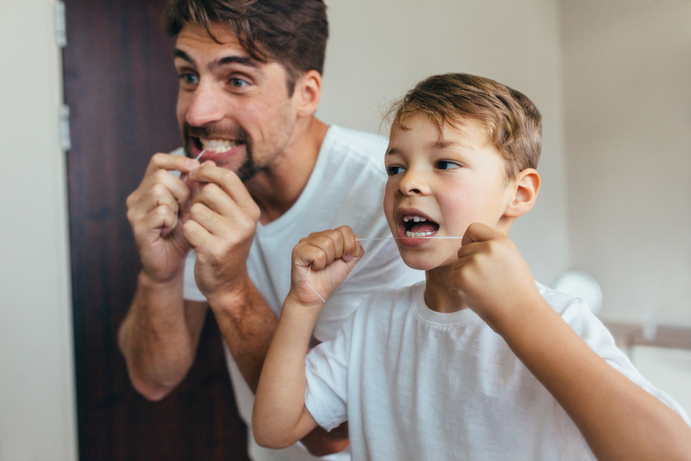 Father and young son flossing together, demonstrating dental habits for children in the article 'At What Age Should My Child Start Flossing?