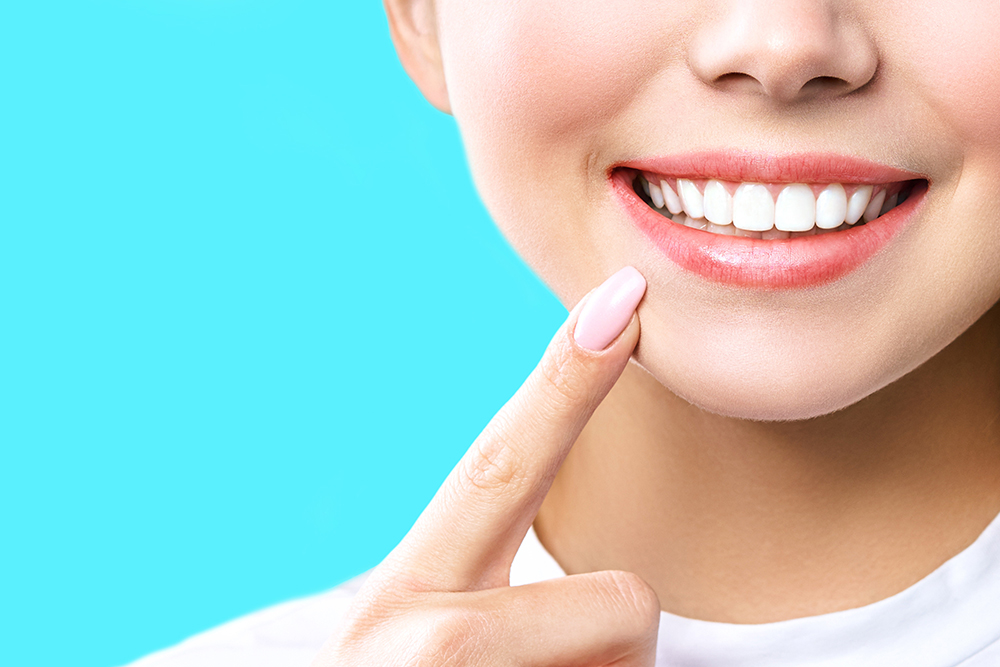 Close-up of a smiling woman pointing to her bright white teeth, representing the effectiveness of teeth whitening products for the blog article 'Which Teeth Whitening Products Work Best!