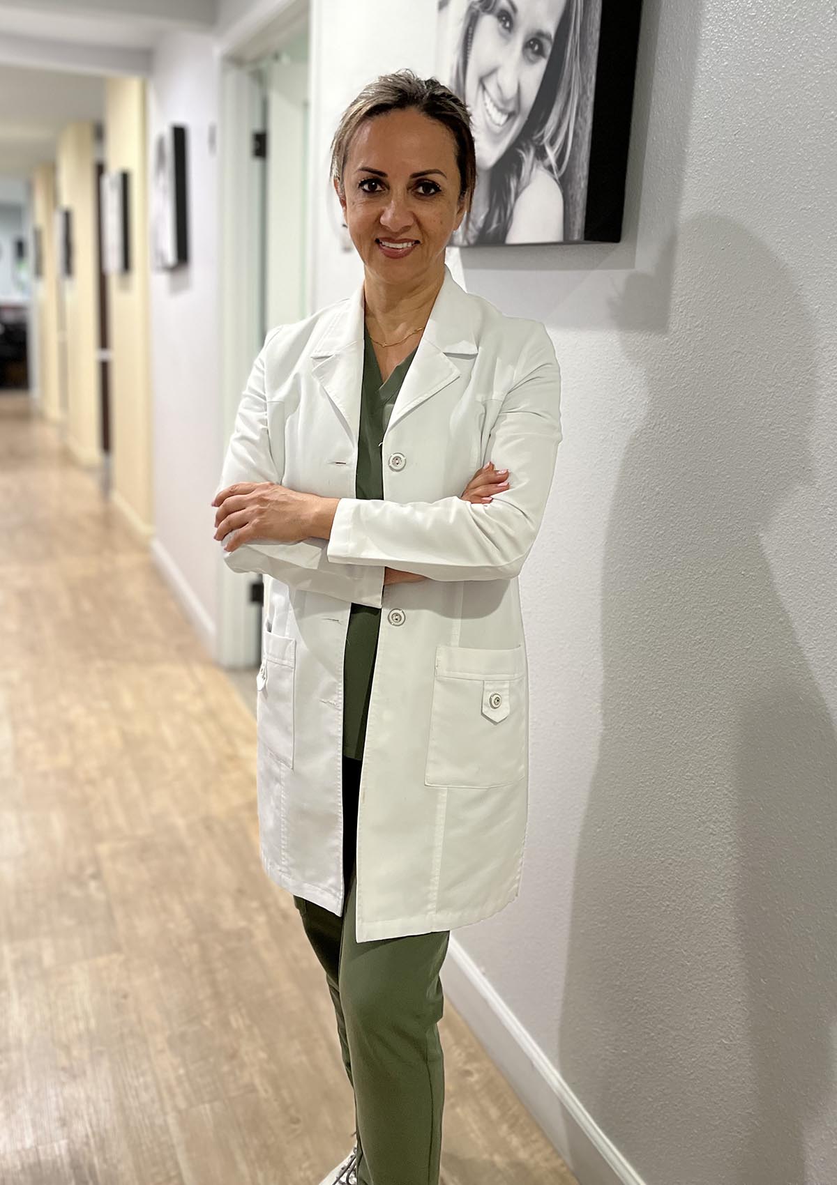 Dr. Marjan Kelishadi standing confidently in her dental clinic wearing a white coat.